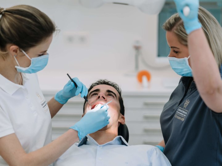 Zahnärtzin und Zahnarztassistenz behandeln einen Patienten