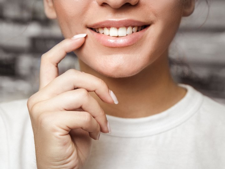 Junge Frau deutet mit ihren Fingern auf ihre gesunden, weißen Zähne